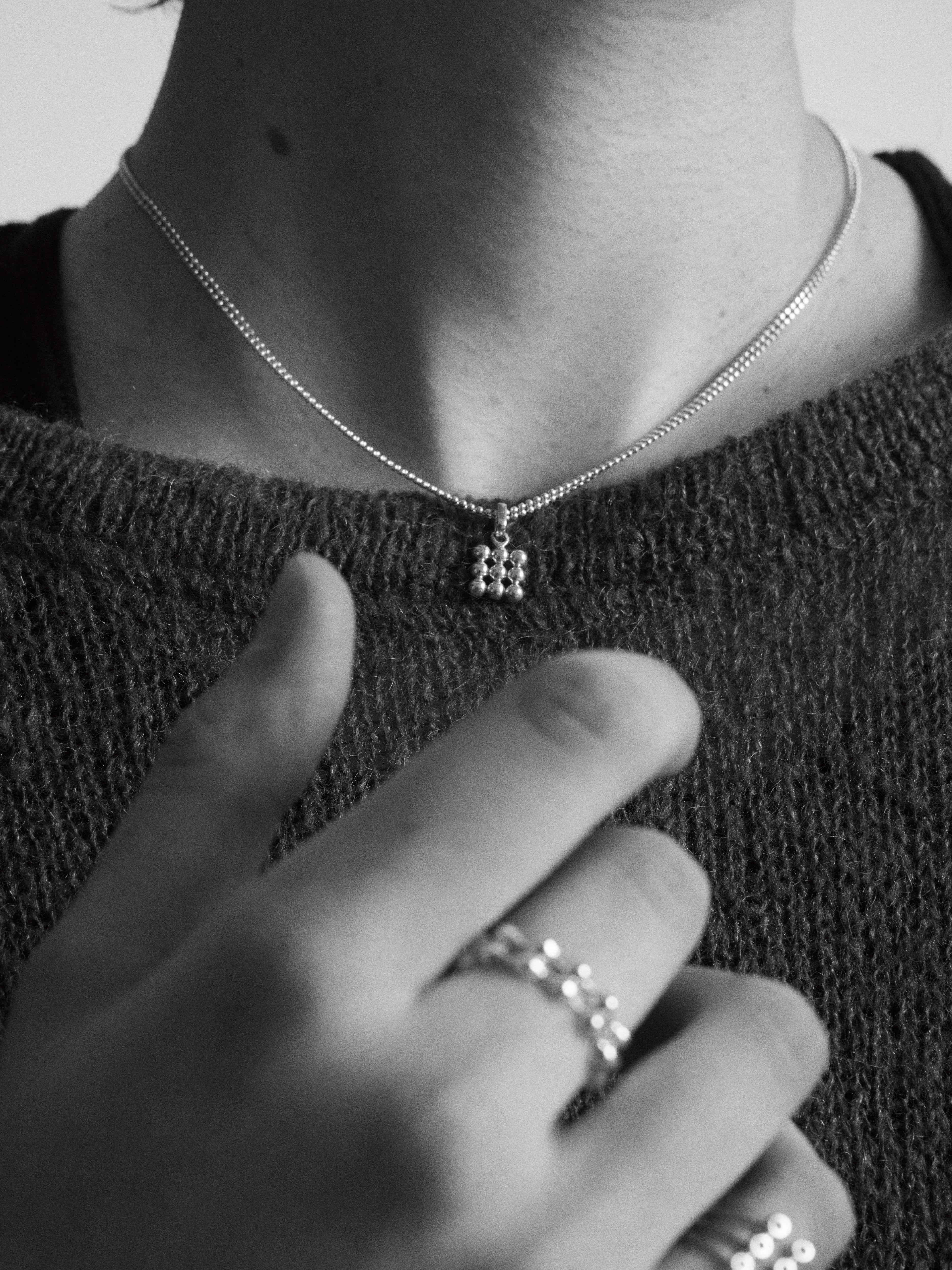 Lifestyle image of a person wearing the grid pendant anddouble row chain styled in a textured knit sweater in a monochromatic style.