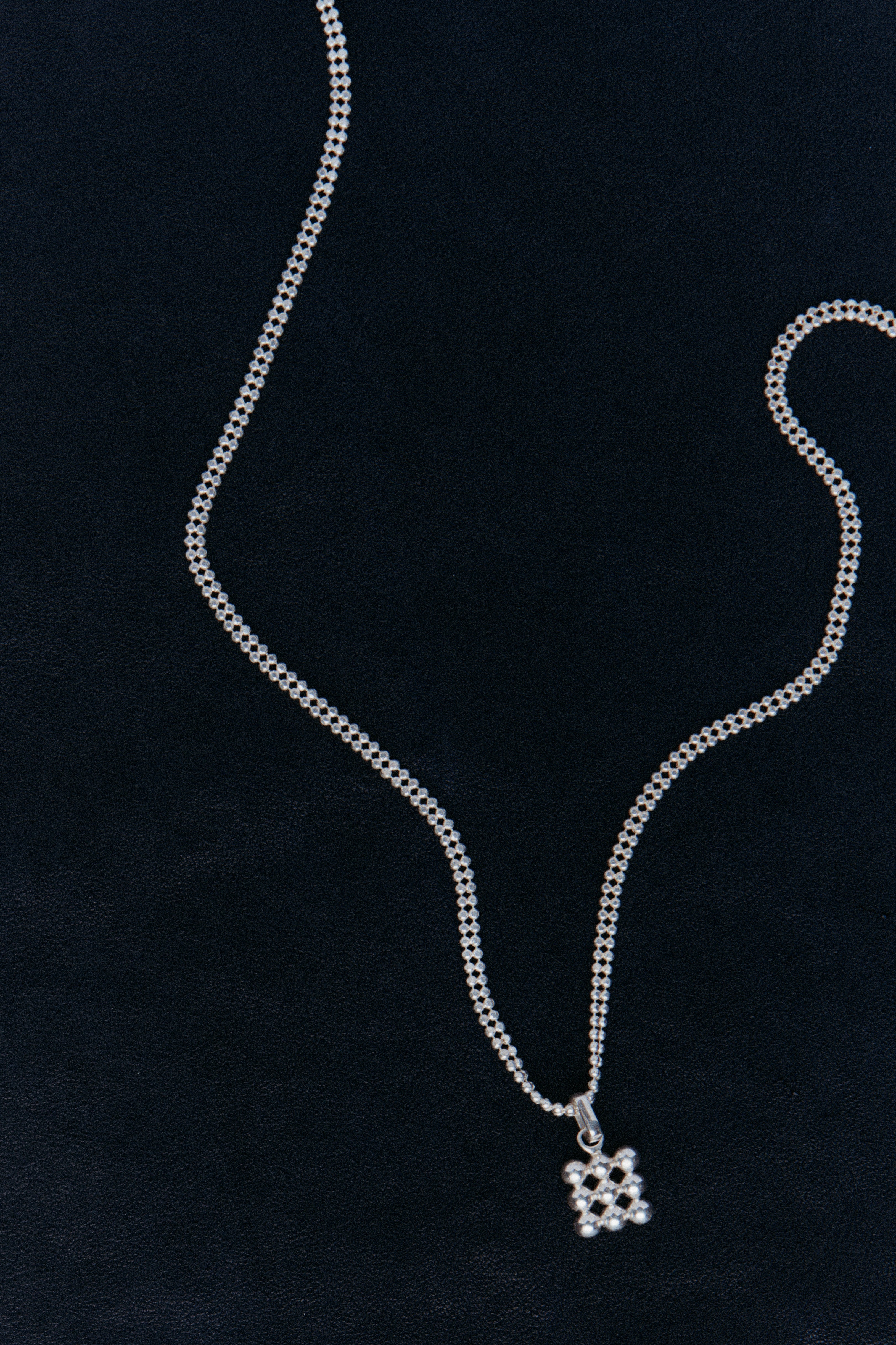 silver double row chain with a small 3x3 silver grid pendant on a dark background.