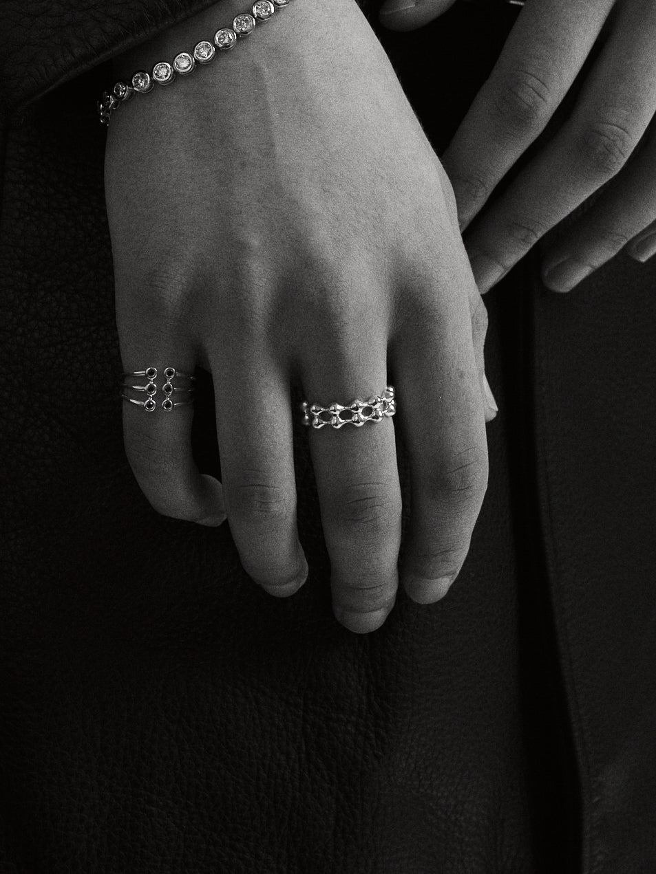 Close-up of a hand wearing the Axis ring, Cage ring and Roller Bracelet in a monochrome style.