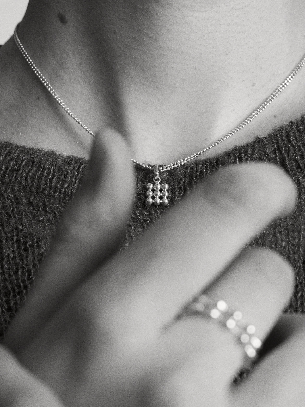 Close-up of a person wearing a silver double row chain with a small 3x3 silver grid pendant styled with rings and a textured top.